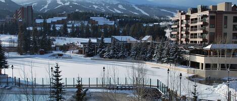 A snow-covered landscape with buildings, a parking area, and a mountain in the background.