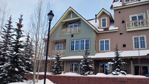A multi-story building with a balcony, snow-covered trees, and a brick wall.