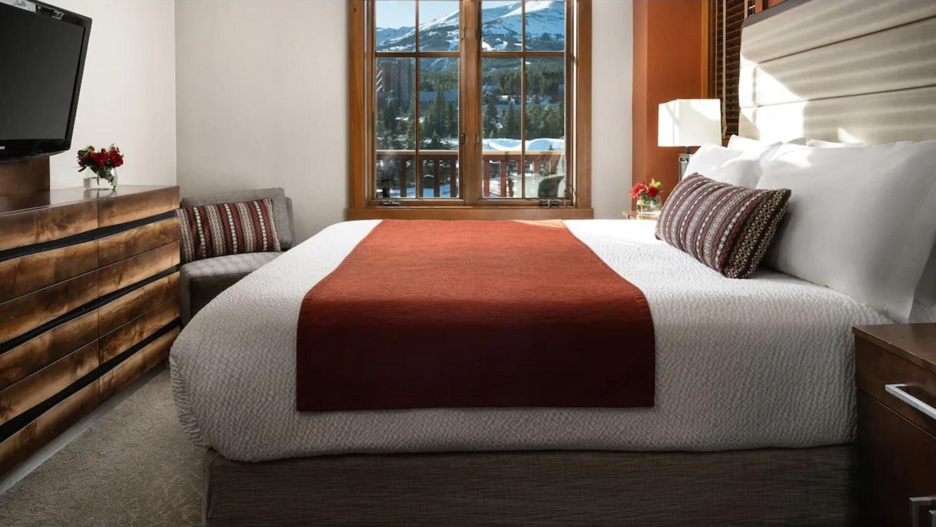 A hotel room with a large bed, a wooden dresser, a TV, and a window with a mountain view.