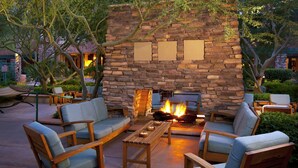 An outdoor seating area with a stone fireplace, lounge chairs, and a fire.