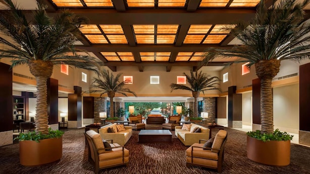 A spacious lobby with a high ceiling, large windows, and a central seating area with sofas and armchairs.