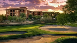 A golf course with bunkers and a building with multiple floors and balconies in the background.