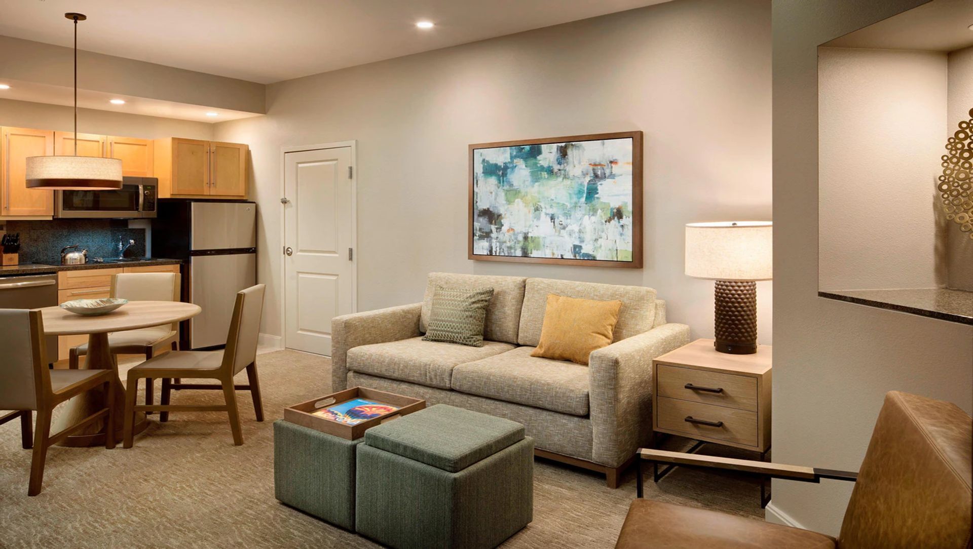 A compact living space with a kitchenette, a sofa, a coffee table, and a painting on the wall.
