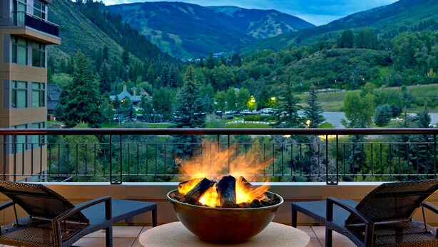 Een balkon met een vuurplaats, rieten stoelen en uitzicht op een bergachtig landschap.