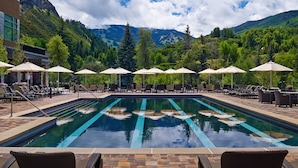 Un espace piscine doté de chaises longues et de parasols, entouré de montagnes et d’arbres.