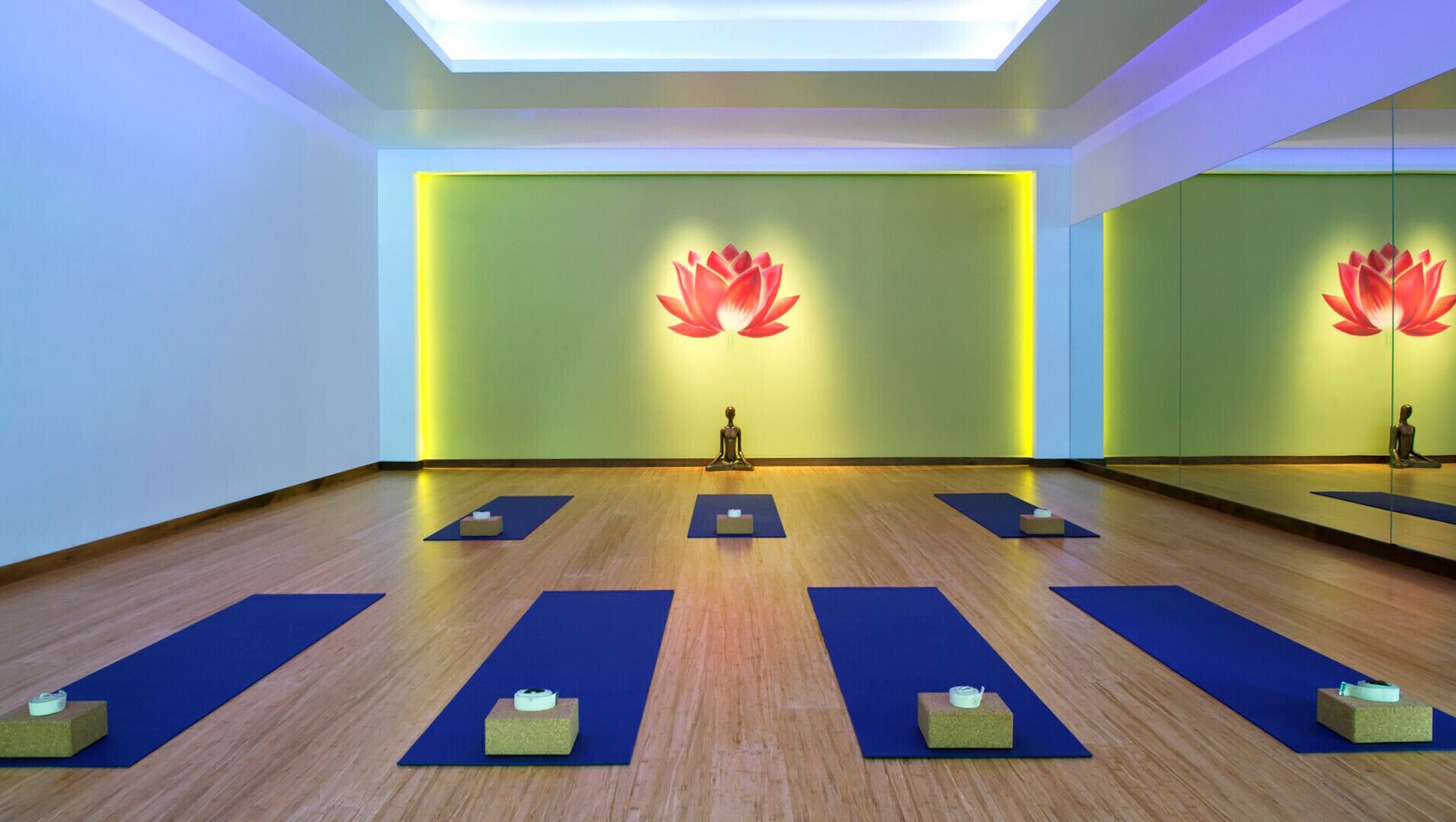 Un studio de yoga doté de planchers en bois, de tapis bleus et d’un symbole de lotus peint sur le mur.