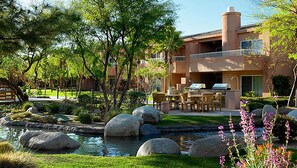 Un jardín ajardinado con un estanque, rocas grandes y mobiliario de exterior.