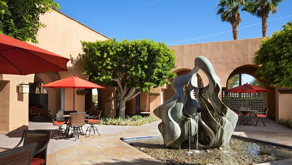 Un patio al aire libre con una fuente, sombrillas rojas y mobiliario exterior.