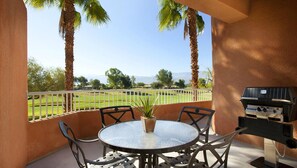 Eine Terrasse mit rundem Tisch und Stühlen, einem Grill und Blick auf einen Golfplatz.