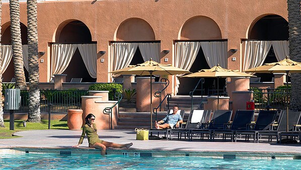 A poolside area with lounge chairs, umbrellas, and a building with arched windows.