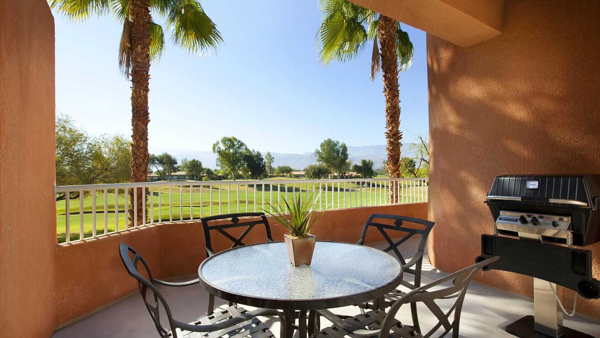 A patio with a round table and chairs, a grill, and a view of a golf course.