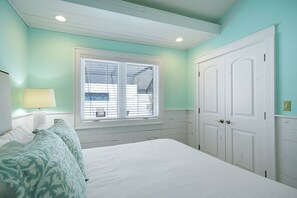 Un dormitorio con cama, una ventana con persianas, una mesita de noche con lámpara y un armario.