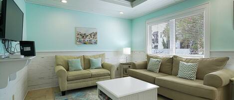 A living room with two beige couches, a white coffee table, and a television on a stand.