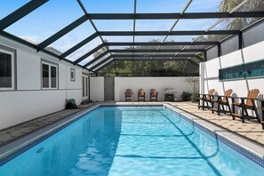 Una piscina con techo de vidrio, rodeada de sillas y una mesita.