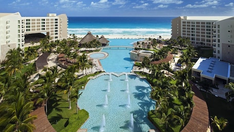 A resort with a central pool, palm trees, and a beach view.