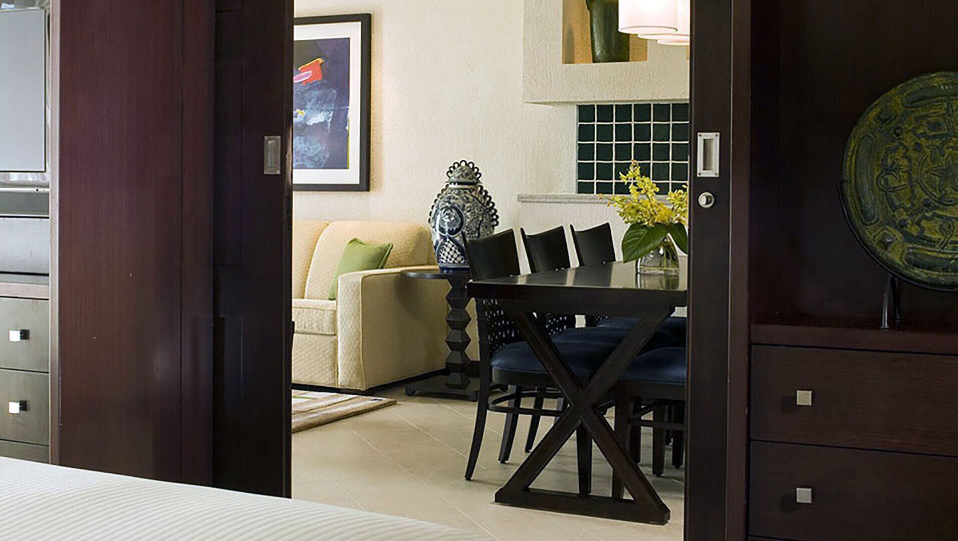 A modern living room with a beige sofa, a dark wooden dining table, and a blue upholstered chair.