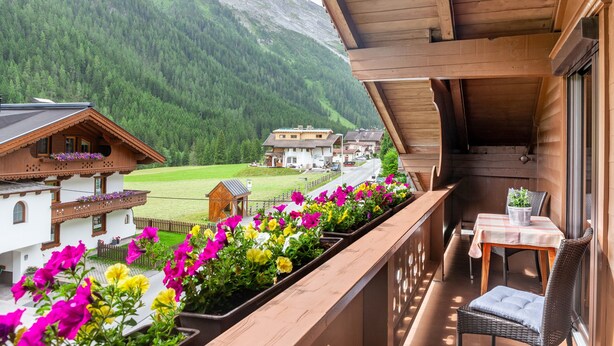 A wooden balcony with a table and chair, overlooking a village and mountains. - "Haus Alpenheim Apartment 1" with Mountain View, Balcony & Wi-Fi (Tux)