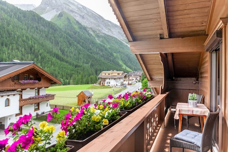 A wooden balcony with a table and chair, overlooking a village and mountains.. "Haus Alpenheim Apartment 1" with Mountain View, Balcony & Wi-Fi