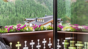 A balcony with a view of a mountain forest, a house with a sloped roof, and a flower bed with pink and yellow flowers. - "Haus Alpenheim Apartment 1" with Mountain View, Balcony & Wi-Fi (Tux)