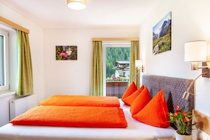 A room with a bed, green curtains, a window, a wall-mounted lamp, and a picture of a mountain. - "Haus Alpenheim Apartment 3" with Mountain View, Balcony & Wi-Fi (Tux)