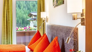 Habitación de hotel con cama, almohadas, ventana con cortinas, una lámpara de pared y un cuadro.