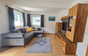 A modern living room with a grey sectional sofa, a small black coffee table, a wooden TV stand, and a large window with curtains. - "Haus Alpenheim Apartment 3" with Mountain View, Balcony & Wi-Fi (Tux)
