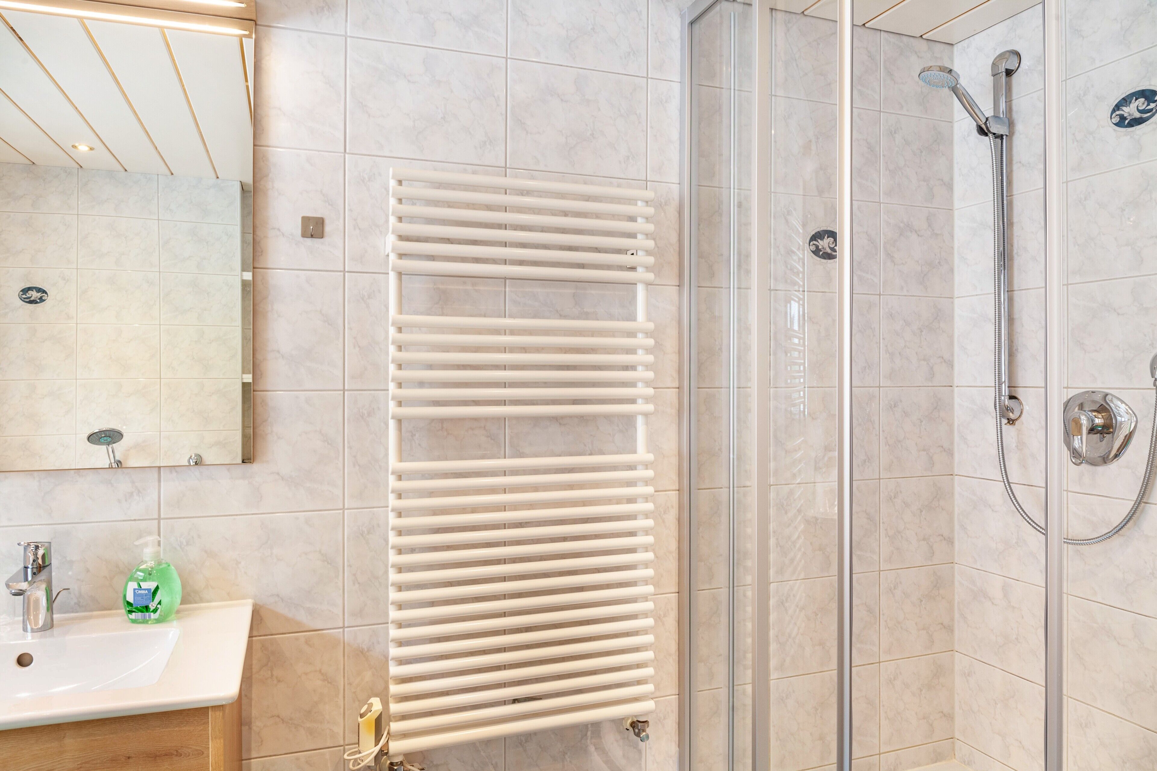 A bathroom with a sink, mirror, towel rack, shower, and tiled walls.