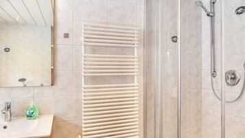 A bathroom with a sink, mirror, towel rack, shower, and tiled walls.