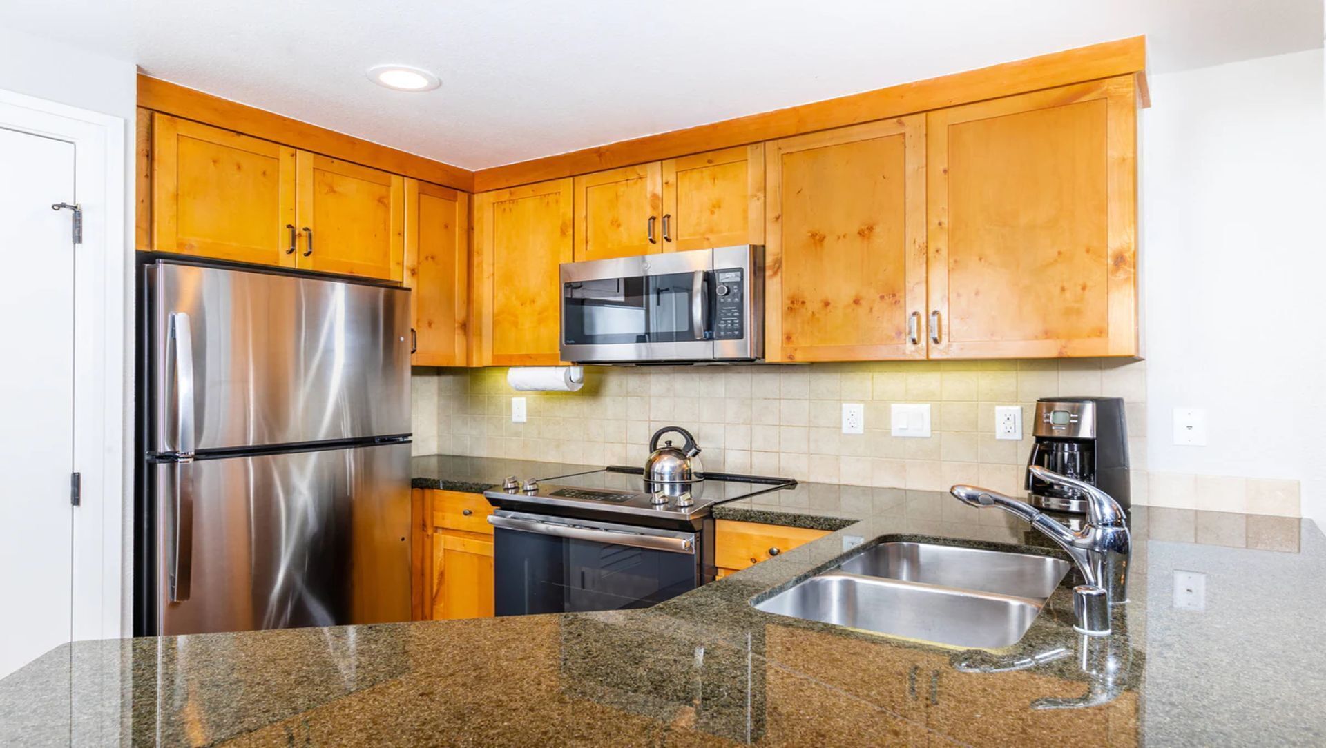 Una cocina moderna con armarios de madera, electrodomésticos de acero inoxidable, encimeras de granito y un microondas integrado.