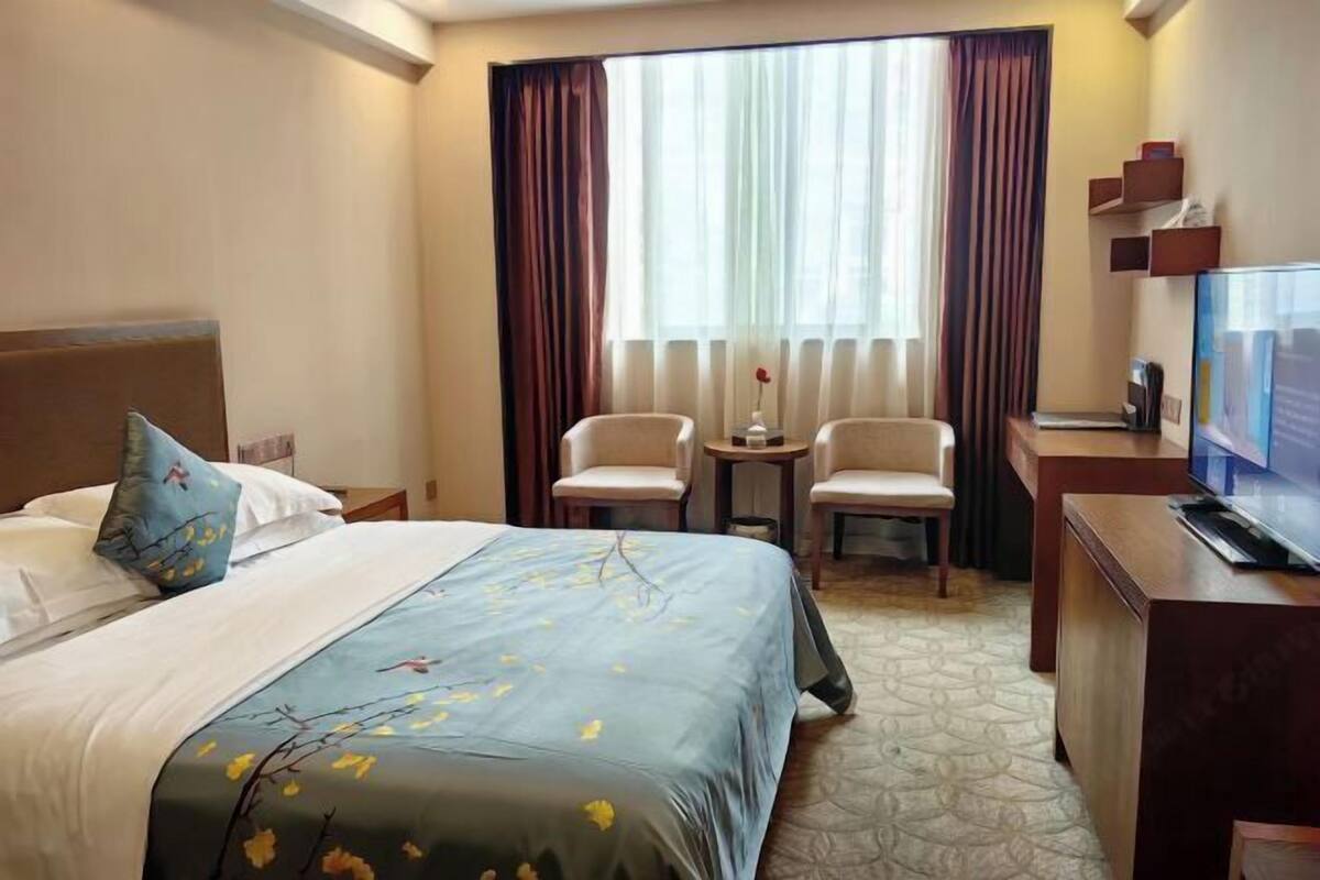 Una habitación de hotel con una cama, dos sillas, una mesita, un televisor y una ventana con cortinas.
