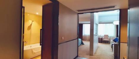 A hotel room with a bathtub, a dining area with a table and chairs, and a living area with a sofa.