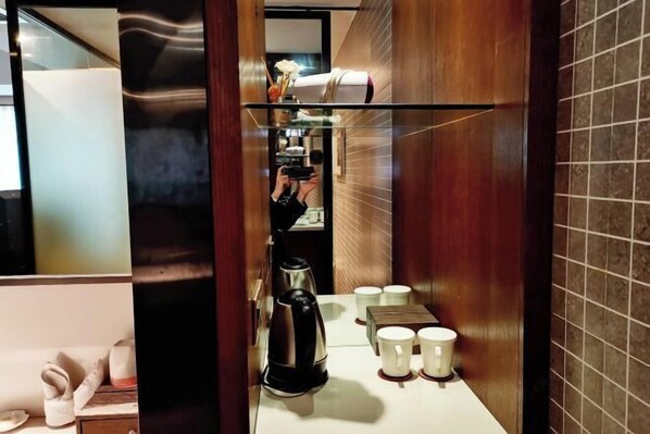 A hotel bathroom with a mirror, a coffee maker, and several cups on the counter. - Feng Du Hotel (Fengdu County)