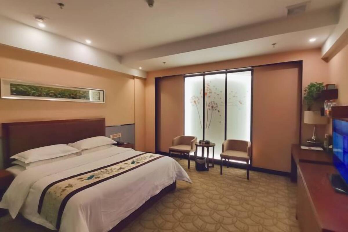 Habitación de hotel con una cama grande, dos sillones, una mesita, televisor y puerta corredera con diseño floral.