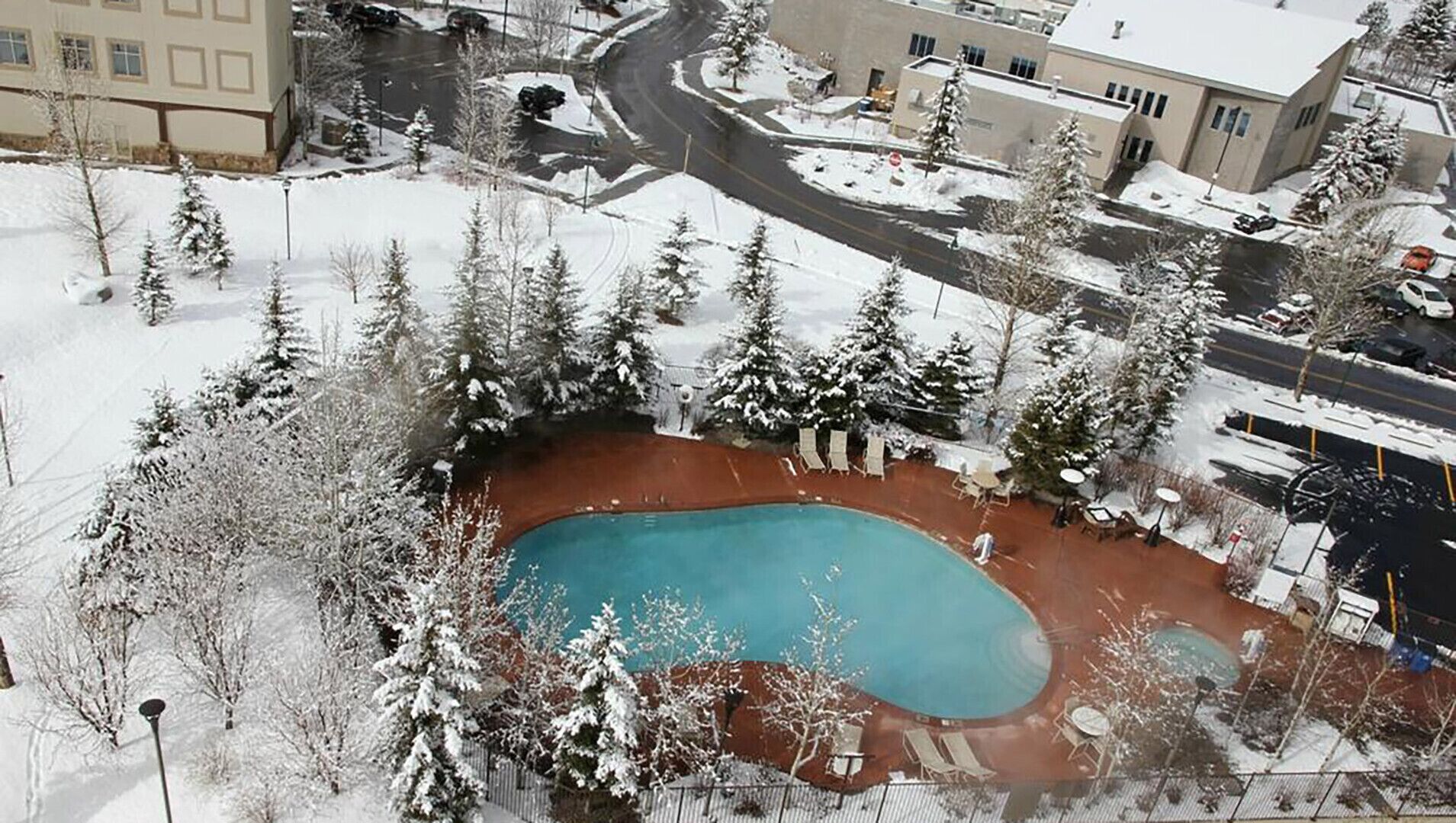 Un espacio exterior nevado con piscina, rodeado de árboles y edificios.
