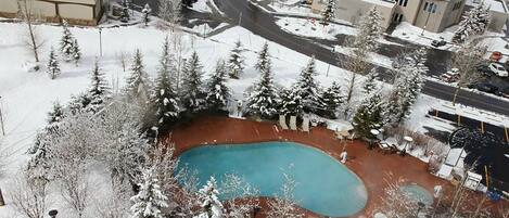 Un espacio exterior nevado con piscina, rodeado de árboles y edificios.