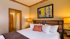 A hotel room with a large bed, a wooden headboard, a painting above the bed, and a door leading to a bathroom. - Studio - Westgate Park City Resort and Spa - Full Resort Access (Park City)