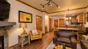 A cozy living room with a fireplace, leather armchairs, a dining area, and a kitchen with wooden cabinets.