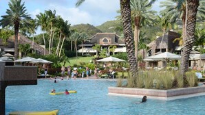 A resort pool area with palm trees, lounge chairs, and a building with a tiled roof.