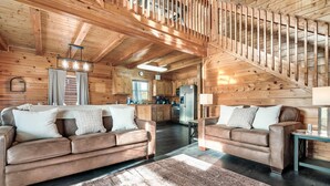 Ein großzügiger Wohnbereich mit zwei braunen Ledersofas, einer Holztreppe und einer Küche im Hintergrund.