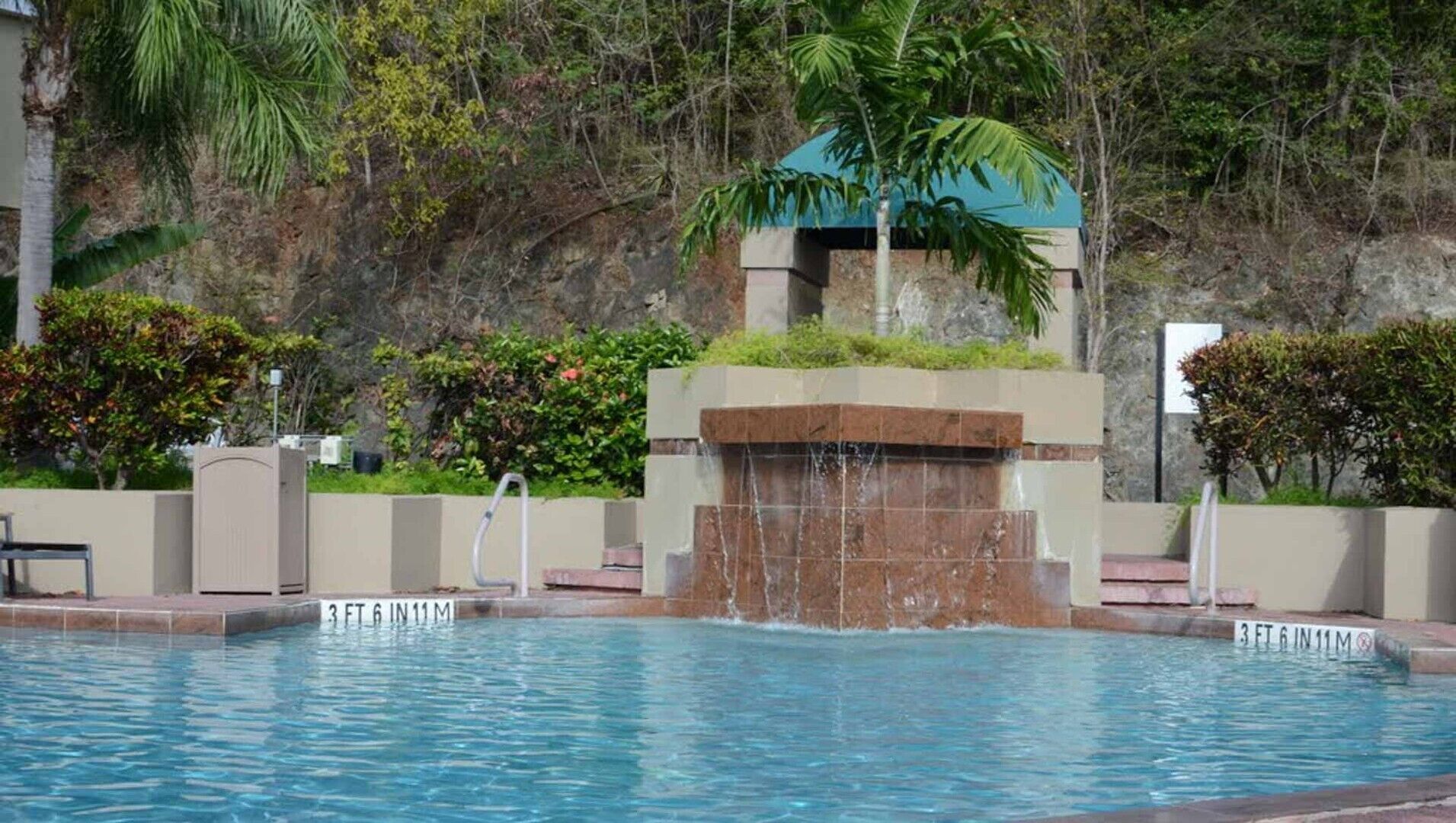 Una piscina con cascata, immersa nel verde e affiancata da un pendio roccioso.