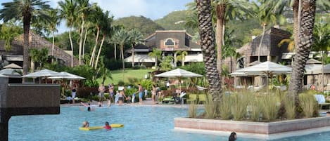 A resort pool area with palm trees, lounge chairs, and a building with a tiled roof.