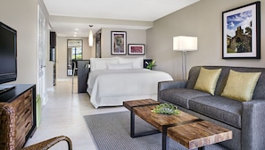 A modern hotel room with a bed, a sofa, a coffee table, and a TV.