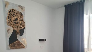A bedroom with a bed, a wall-mounted artwork, a bedside table, and a window with curtains. - Modern 1 Bed Seafront Apt Los Boliches (Fuengirola)