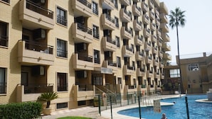 A multi-story building with balconies, a swimming pool, and a palm tree. - Modern 1 Bed Seafront Apt Los Boliches (Fuengirola)