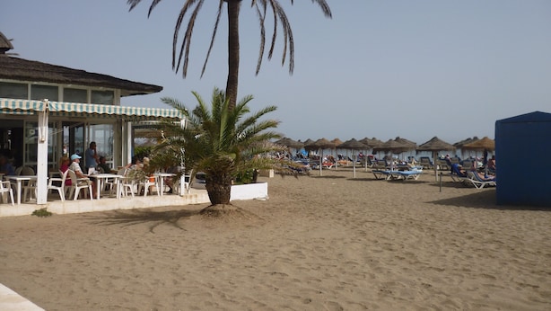 A beachside restaurant with outdoor seating, palm trees, and beach umbrellas. - Modern 1 Bed Seafront Apt Los Boliches (Fuengirola)