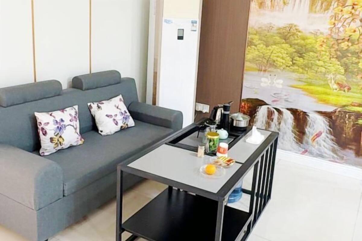 A modern living room with a grey sofa, floral cushions, a small black coffee table, and a mural of a waterfall.