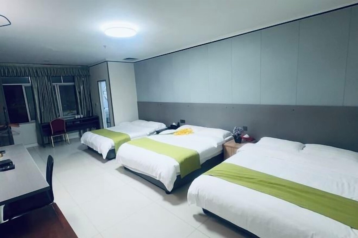 A hotel room with three beds, a desk, and a chair.