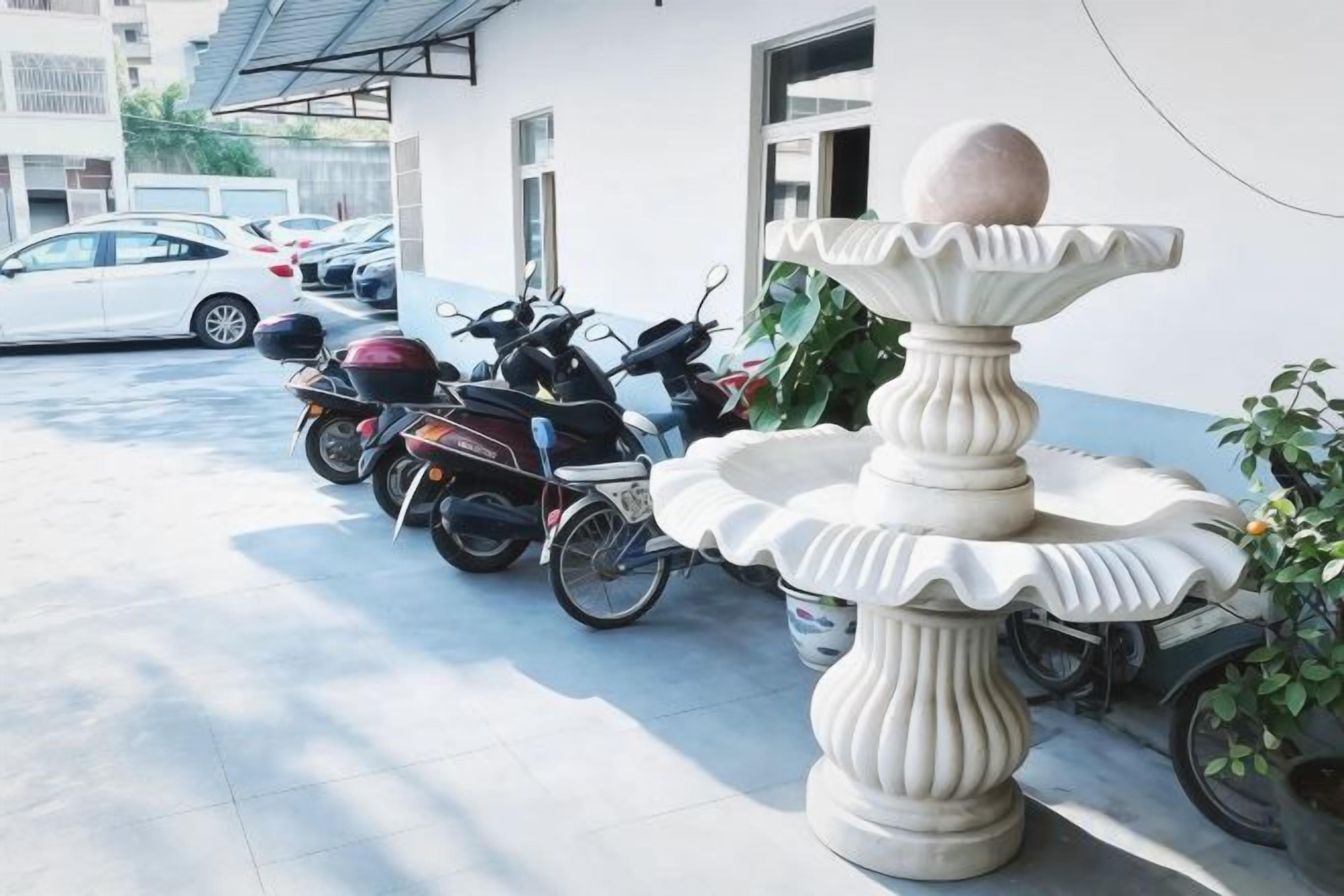 Un estacionamiento con una fuente decorativa, un edificio blanco y motocicletas estacionadas.