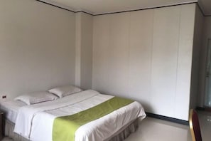 A single bed with white bedding and a green accent, a small bedside table, and a plain wall with a door. - Shengtai Hotel (Boluo)
