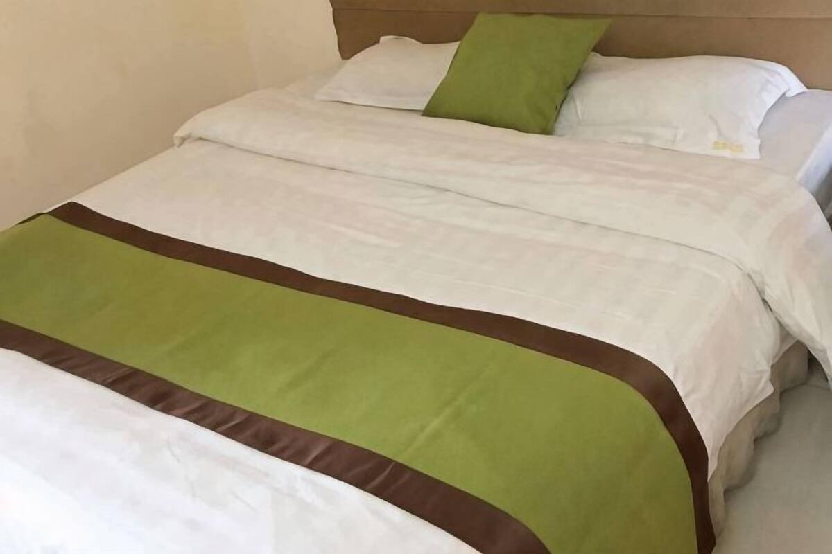 A bed with white bedding and a green and brown accent.